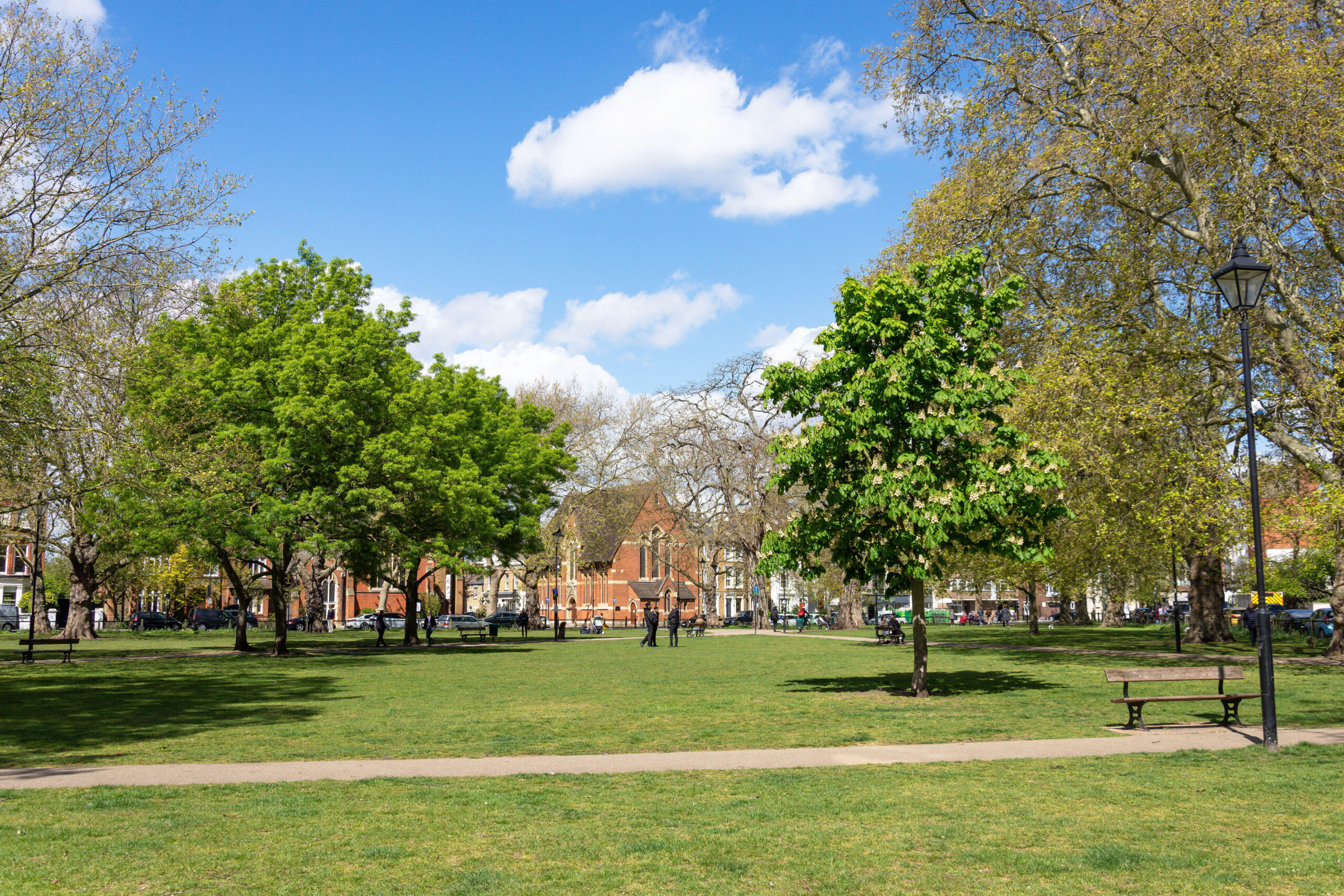 A sun-drenched view of the iconic Parsons Green in Fulham, London, showing the expansive green space, mature trees, and traditional Victorian architecture that defines the local neighborhood.