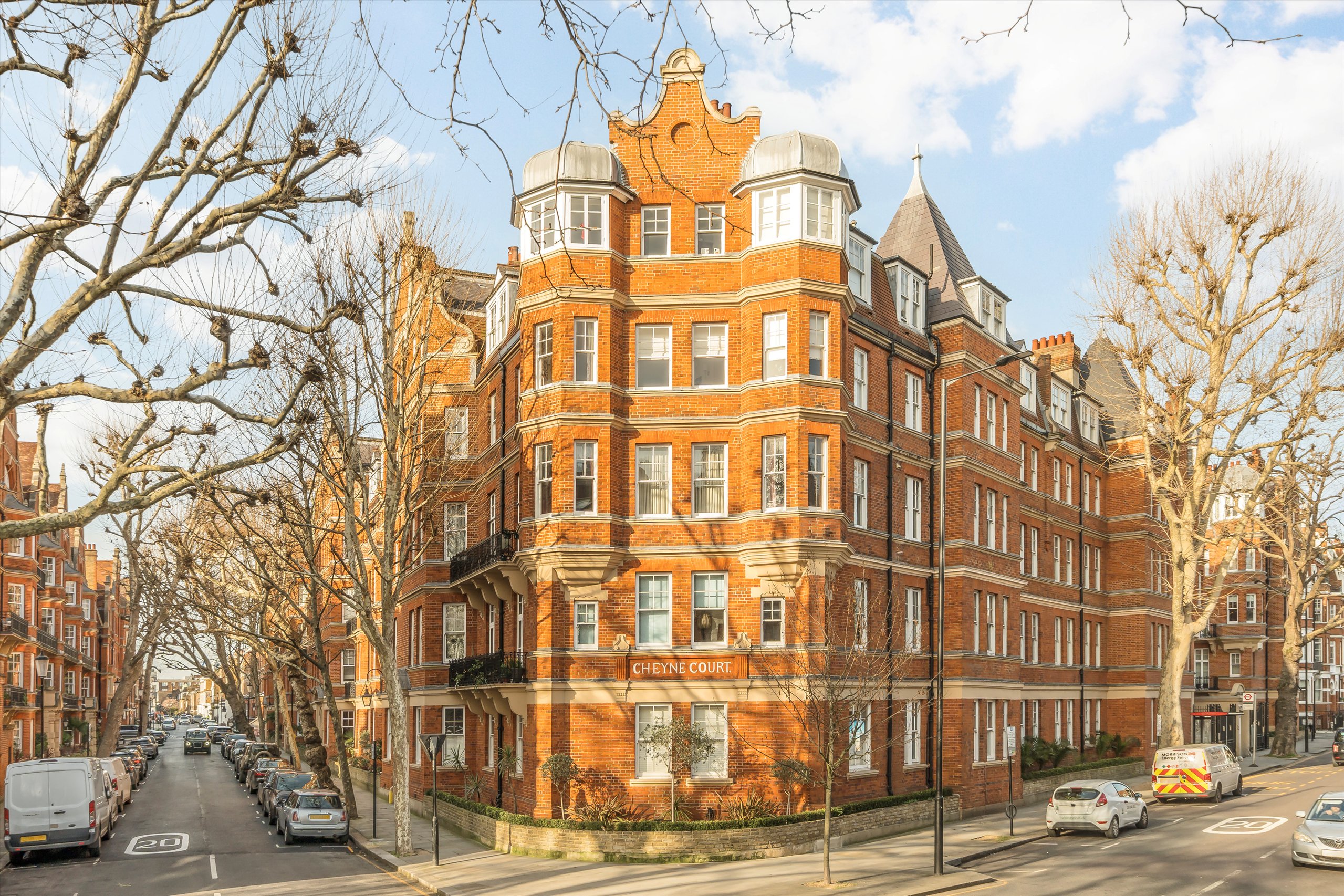 Exterior view of Cheyne Court, a historic red-brick mansion block building on a tree-lined street corner in Chelsea, London
